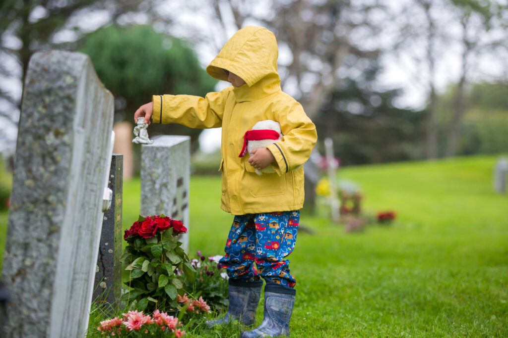 Junde mit gelber Regenjacke auf dem Friedhof vor Grabstein