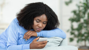 Frau auf Sofa schaut traurig auf ihr Handy